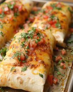 two burritos on a baking sheet with tomatoes and cilantroo garnishes