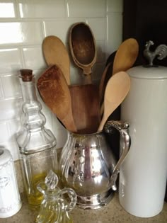 wooden spoons and other kitchen utensils in a silver pitcher on a counter