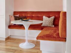 an orange couch and table in a room with wood flooring, white walls and wooden floors