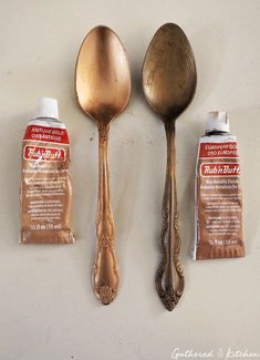 three spoons and two bottles of toothpaste on a white counter top with gold paint