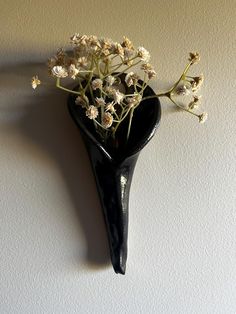 a black vase with flowers in it hanging on the wall next to a white wall