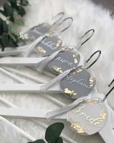 three white and gold wedding hangers with personalized tags on them, along with greenery