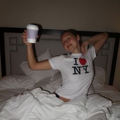 a woman laying in bed with her arms up and holding a coffee cup to her chest