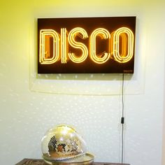 a disco ball sitting on top of a wooden table next to a neon sign that reads disco