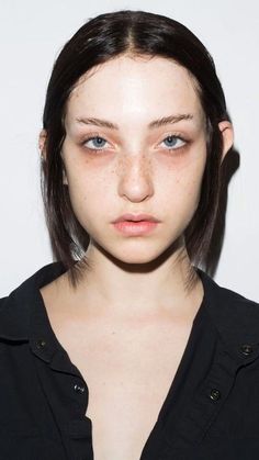 a young woman with freckles on her face looking at the camera while standing in front of a white background