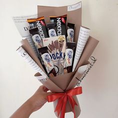 a hand holding a bouquet of chocolates and candy bar wrapped in brown paper with a red ribbon