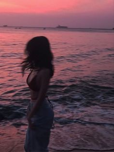 a woman standing on top of a sandy beach next to the ocean at sunset or dawn