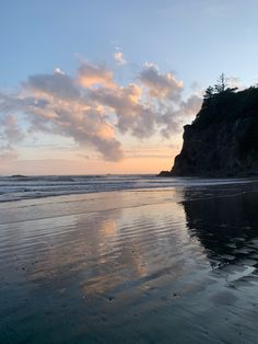 the sky is reflected in the wet sand by the water's edge at sunset