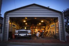 a truck is parked in front of a garage with its doors open and two people inside