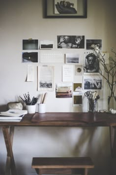 a wooden table topped with a vase filled with flowers next to a wall covered in pictures