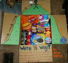 a cardboard box filled with candy and snacks on top of a carpeted floor next to a sign that says we're 17 way