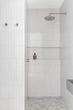 a white tiled bathroom with a shower head and hand held shower faucet in the corner