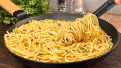 a pan filled with spaghetti being stirred by a spatula on top of a wooden table