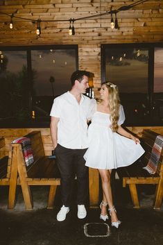 a man and woman standing next to each other in front of a wooden table with chairs