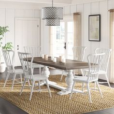 a dining room table with white chairs and a potted plant on the rug in front of it