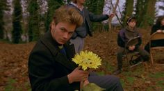 three people sitting in the woods and one is holding a flower