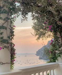 an open balcony overlooking the ocean with pink flowers on it and greenery hanging from the ceiling