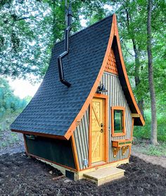 a small wooden house in the woods with a black roof and brown shingles on it