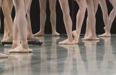 several ballet dancers standing in a row with their feet on the ground and one person's leg up