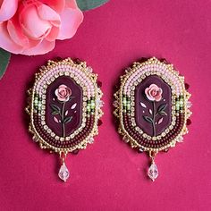 two pieces of jewelry sitting on top of a pink surface next to a rose flower