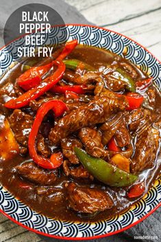 a bowl filled with beef and peppers on top of a wooden table