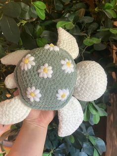 a crocheted turtle with daisies on it's shell in front of a plant