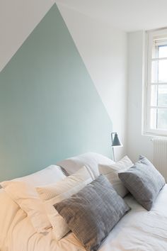 a bed with white sheets and pillows in front of a blue accent wall that has a triangle design on it