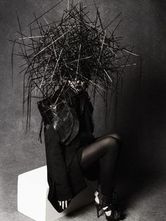 black and white photograph of a woman sitting on a stool with lots of sticks sticking out of her head