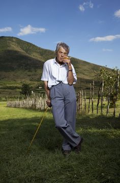 an old man standing in the grass with his hand on his chin and looking at the camera