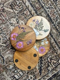 three wooden coasters with flowers painted on them sitting on a carpeted area next to a rug