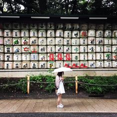 a woman with an umbrella is walking in front of a wall that has cans on it