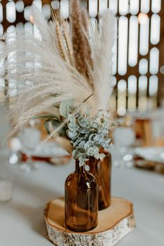 two vases with flowers and feathers are on a wooden stand at the head table