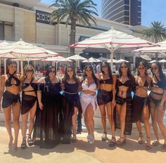 a group of women standing next to each other in front of a pool with umbrellas