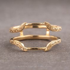 two gold rings with designs on them sitting on a table next to a gray surface