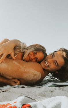 a man and woman laying on top of a sandy beach next to the ocean with their arms around each other