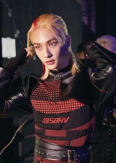 a woman with blonde hair wearing a black and red leather outfit while holding her hands on her head