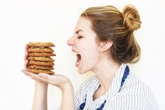 a woman holding a stack of cookies in front of her face and making a funny face