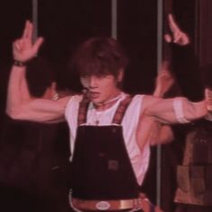 a man in overalls and suspenders holding his hands up while standing on stage