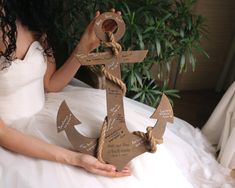 a woman in a white dress holding up a wooden anchor with names and arrows on it