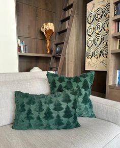 two green pillows sitting on top of a white couch next to a book shelf filled with books