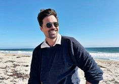 a man standing on top of a sandy beach next to the ocean with his hands in his pockets