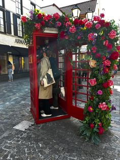 a woman is standing in a red phone booth with flowers on the outside and inside