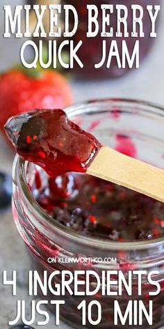 a jar filled with mixed berry jam on top of a wooden spoon next to an apple