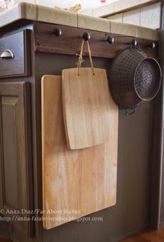 a wooden cutting board mounted to the side of a kitchen cabinet with pots and pans hanging on it