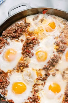 three eggs are cooking in a skillet with ground beef and cheese on the side