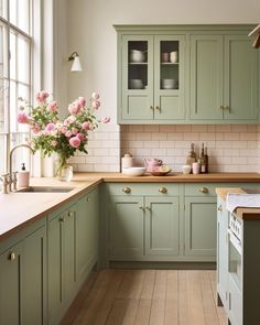 a kitchen filled with lots of green cabinets next to a counter topped with pink flowers