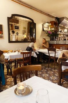 people sitting at tables in a restaurant with white tablecloths and brown wooden chairs