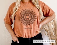 a woman standing in front of a wall wearing an orange t - shirt with a sun design on it