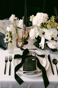 the table is set with white flowers and black ribbon, silverware and napkins