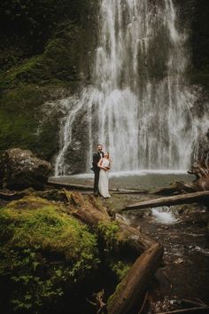 a bride and groom standing in front of a waterfall